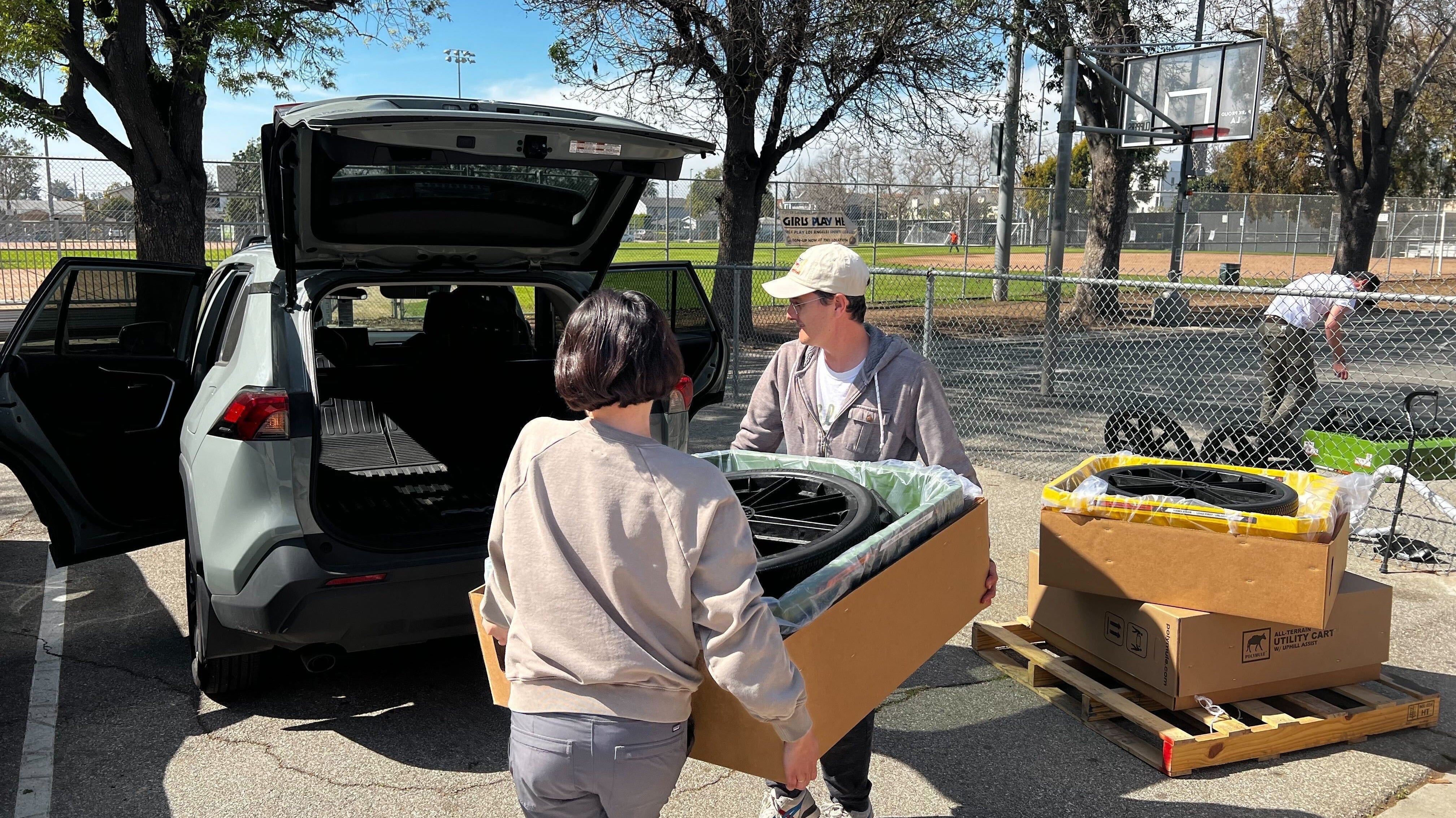 A couple load a boxed-up Polymule cart into the trunk of their SUV.