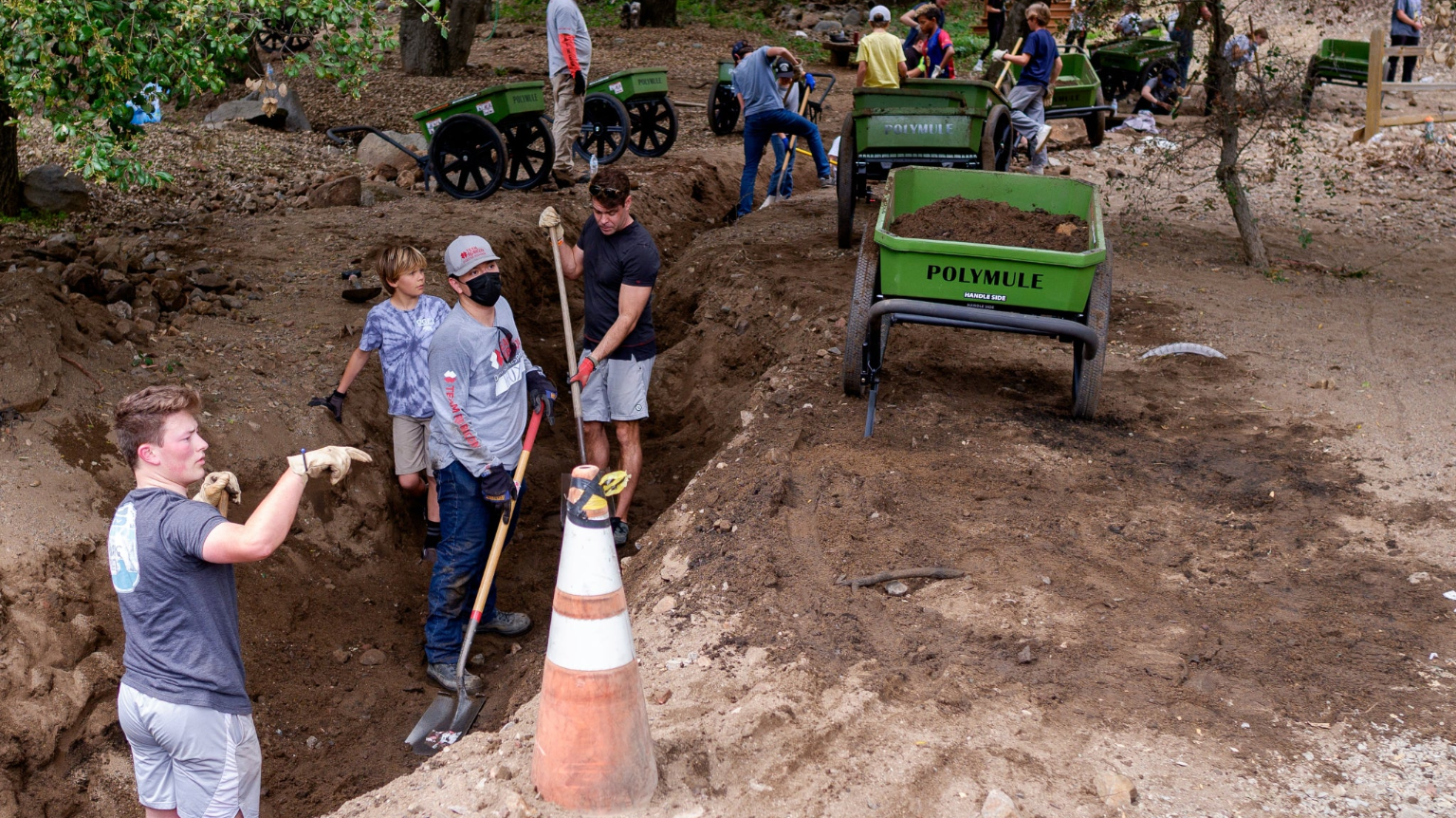 Volunteers use shovels and Polymule carts to clear a stream bed.