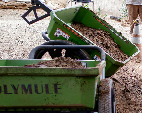 Two Warrior carts sit side by side filled with dirt. One cart is tipped up to dump the dirt.