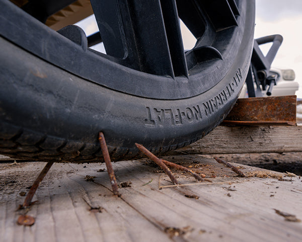 Close up of a no-flat tire. The tire rolls over nails, which stick up from a wood board.