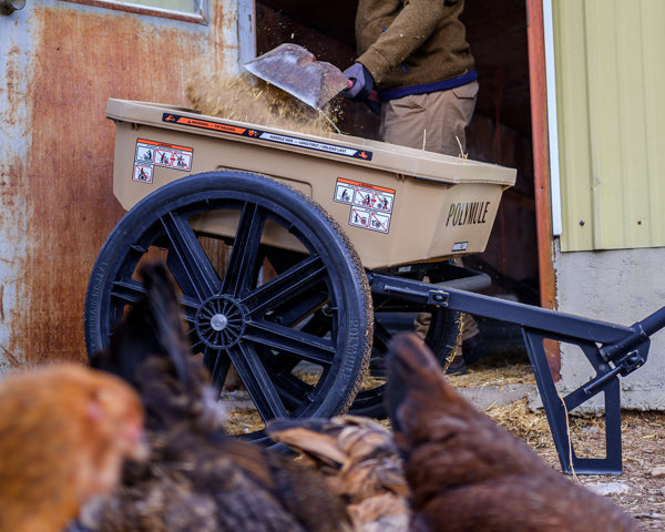 Worker shovels hay from a chicken coop into a Warrior cart as chickens roam nearby.