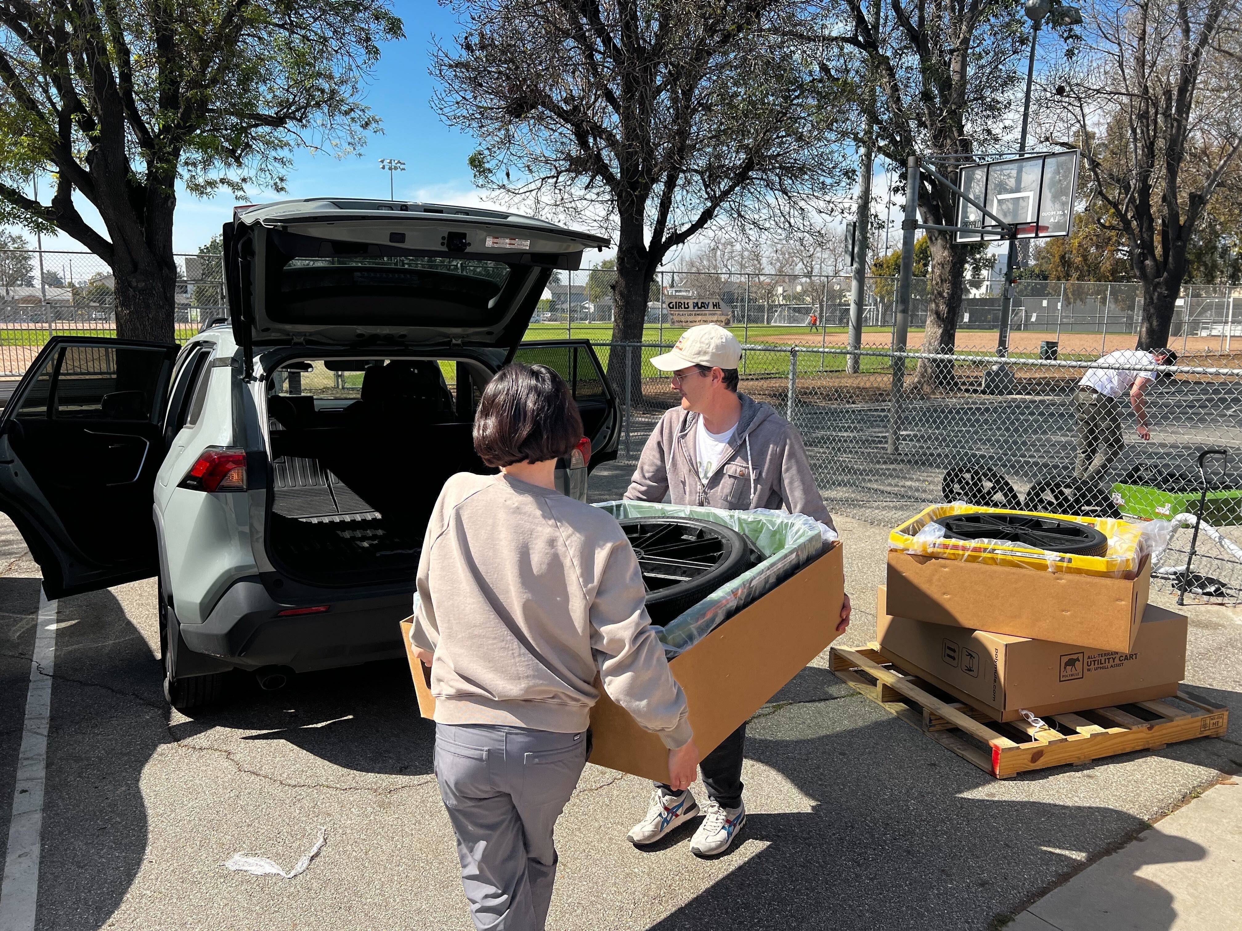 A couple load a boxed-up Polymule cart into the trunk of their SUV.