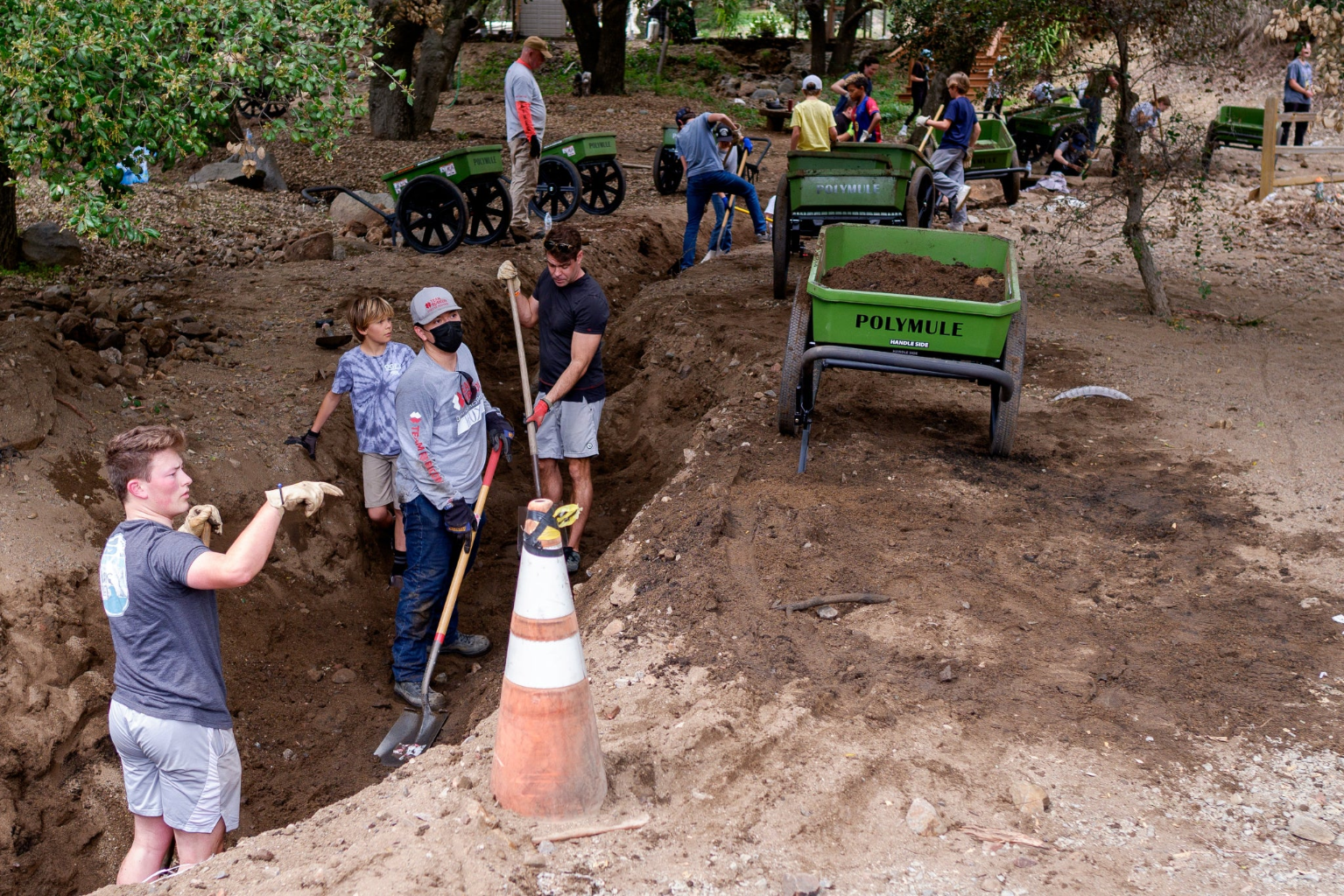 Volunteers use shovels and Polymule carts to clear a stream bed.