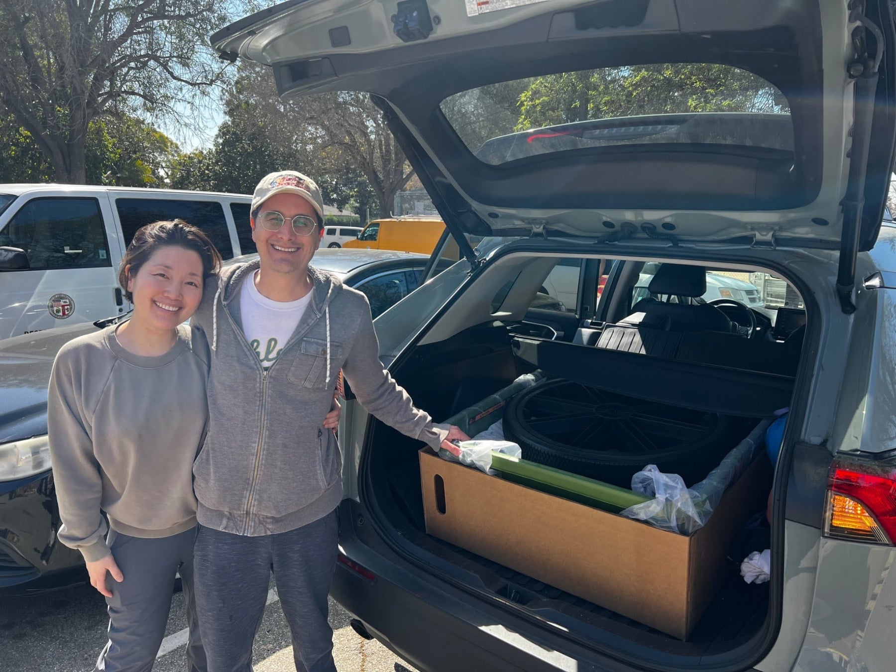 Two people smiling and standing next to their car's open trunk with a Polymule cart inside