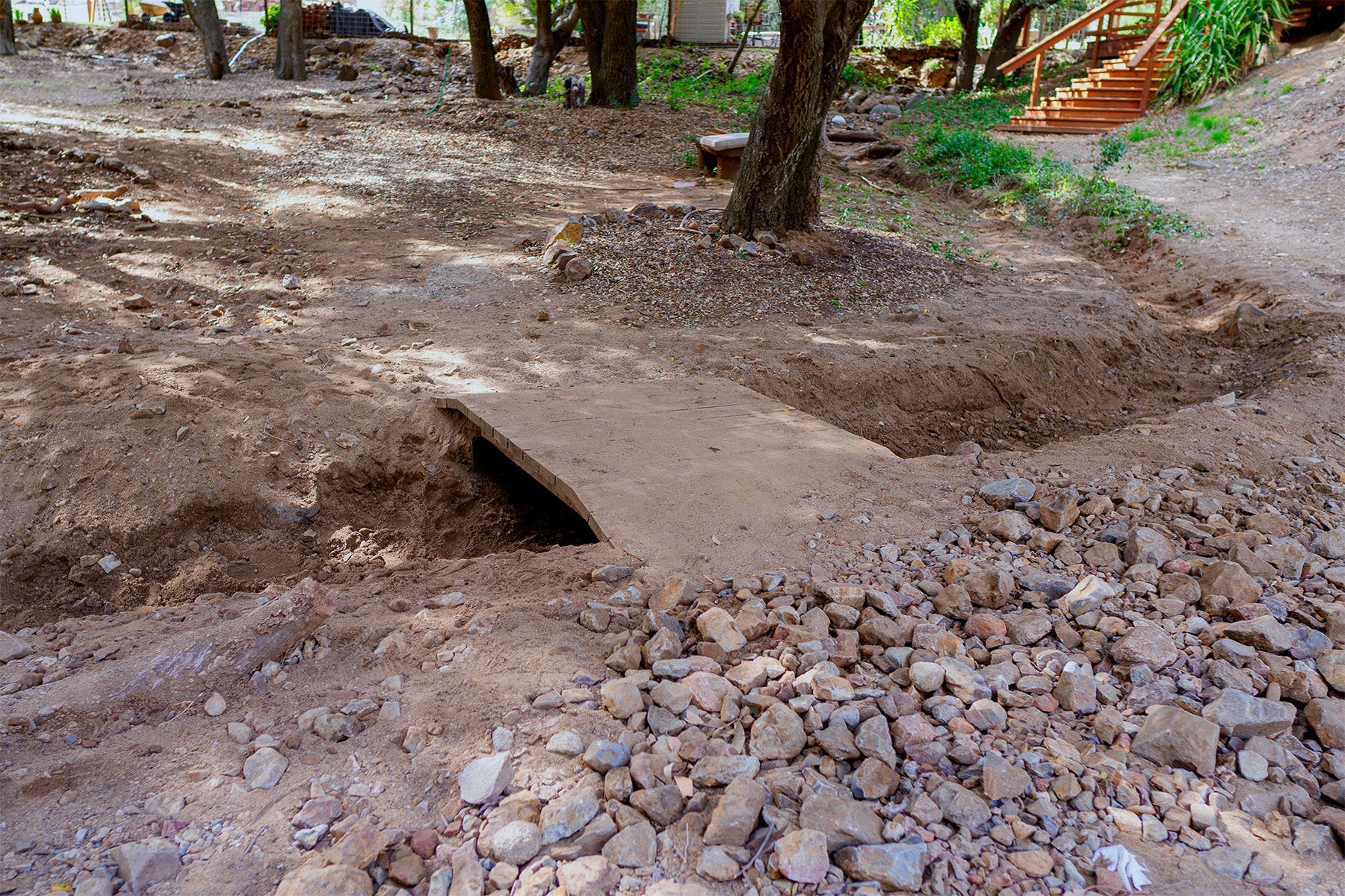 Recently dug up dry creek bed with a wooden bridge in a wooded area
