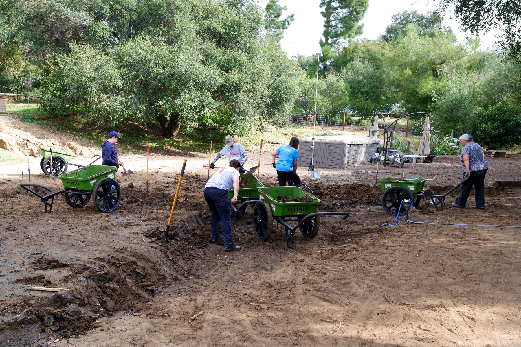 Volunteers working with Polymule carts to clear mud from a yard