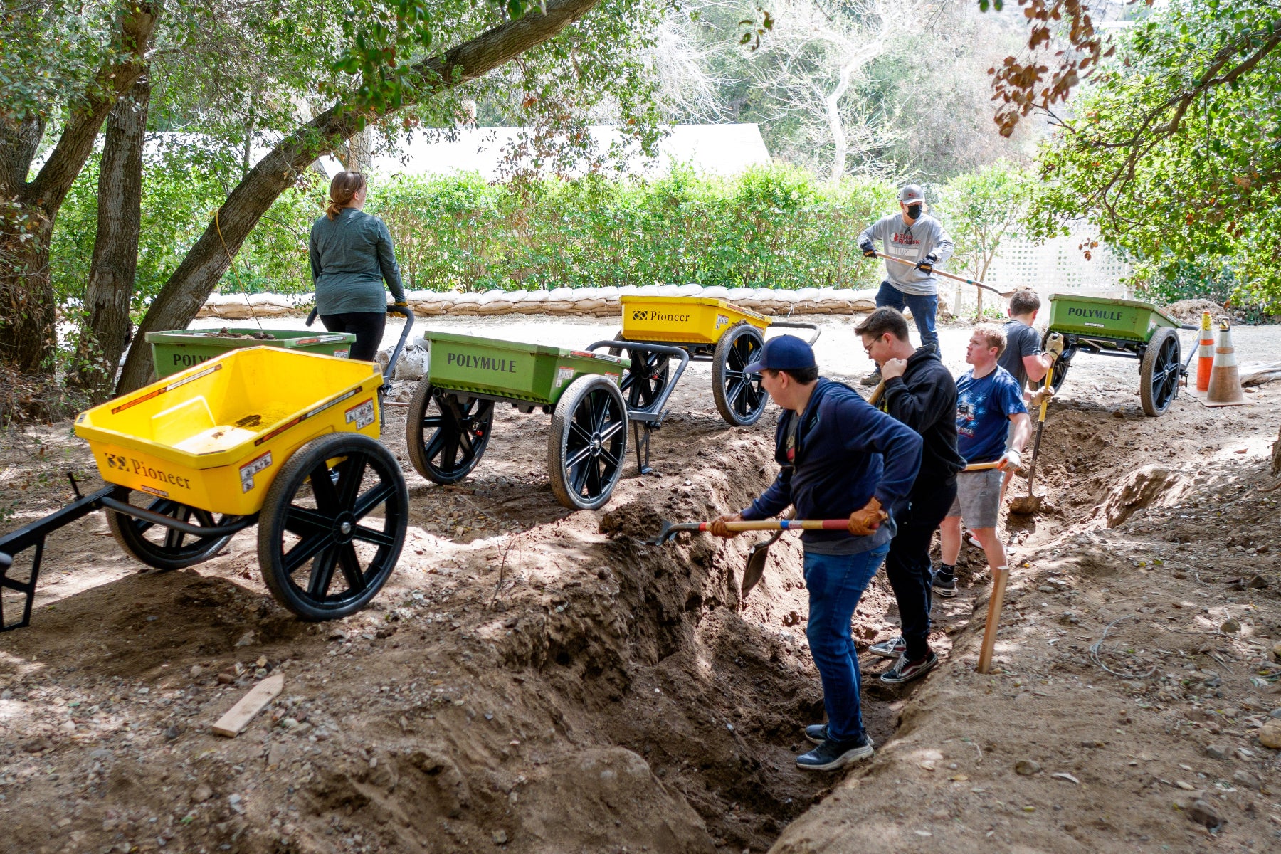 Volunteers working with shovels and Polymule carts to clear a creek bed