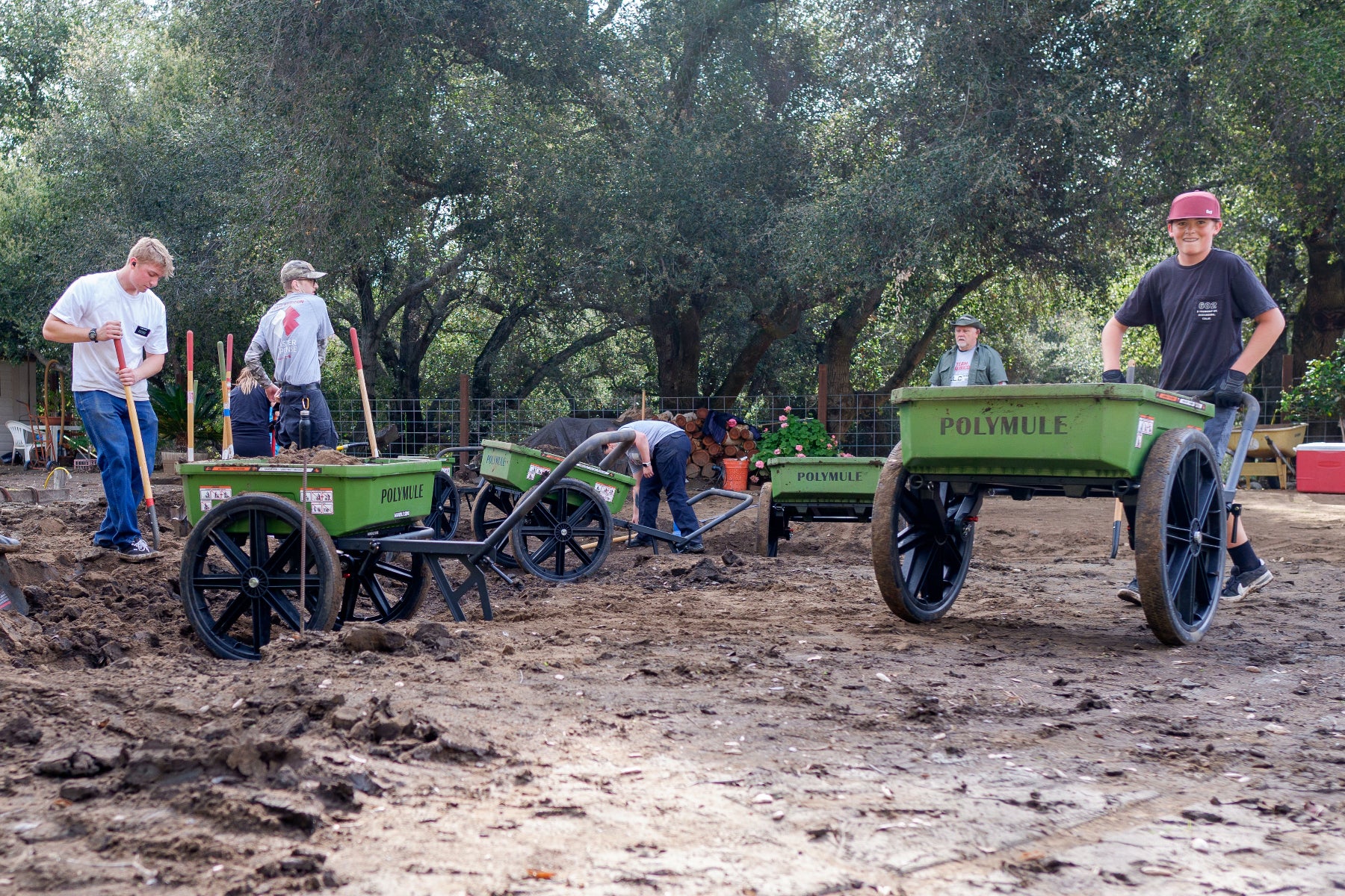 Volunteers working with shovels and Polymule carts to clear mud from a yard