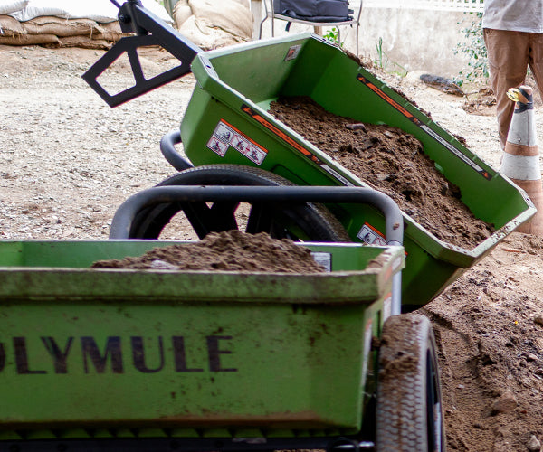 Two Warrior carts sit side by side filled with dirt. One cart is tipped up to dump the dirt.