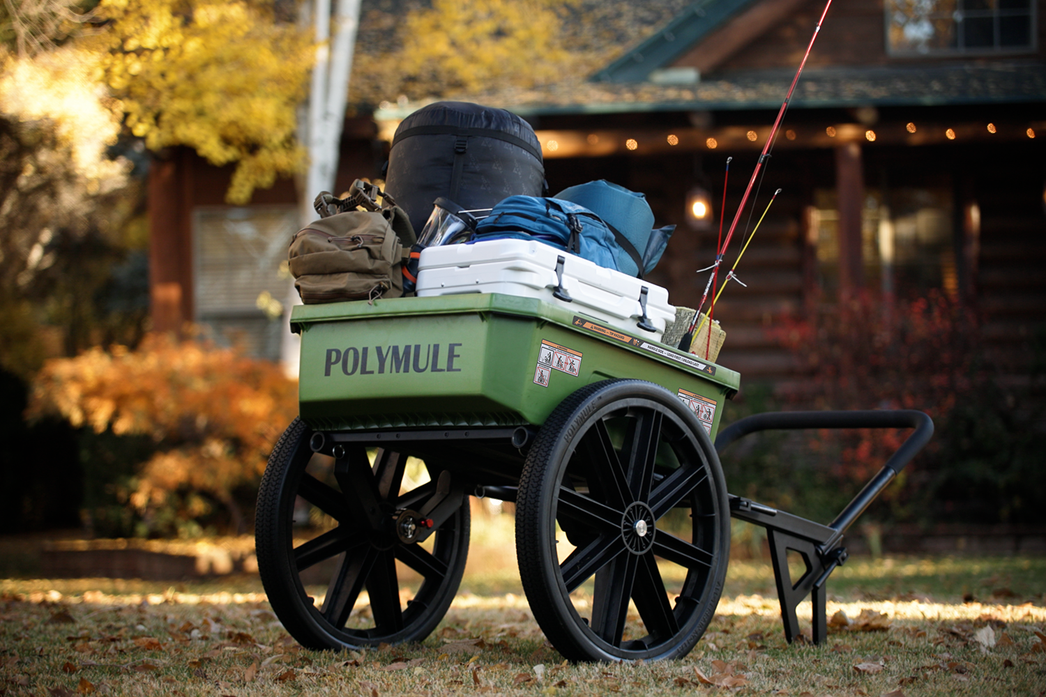 A Polymule Warrior utility cart filled with camping gear sits in front of a cabin in the forest.
